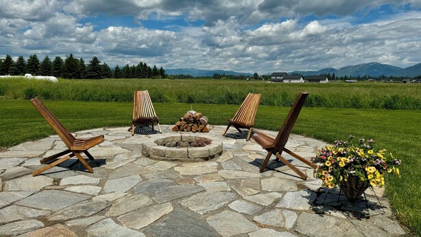 An outdoor seating area with stone flooring, a fire pit, and three wooden chairs.