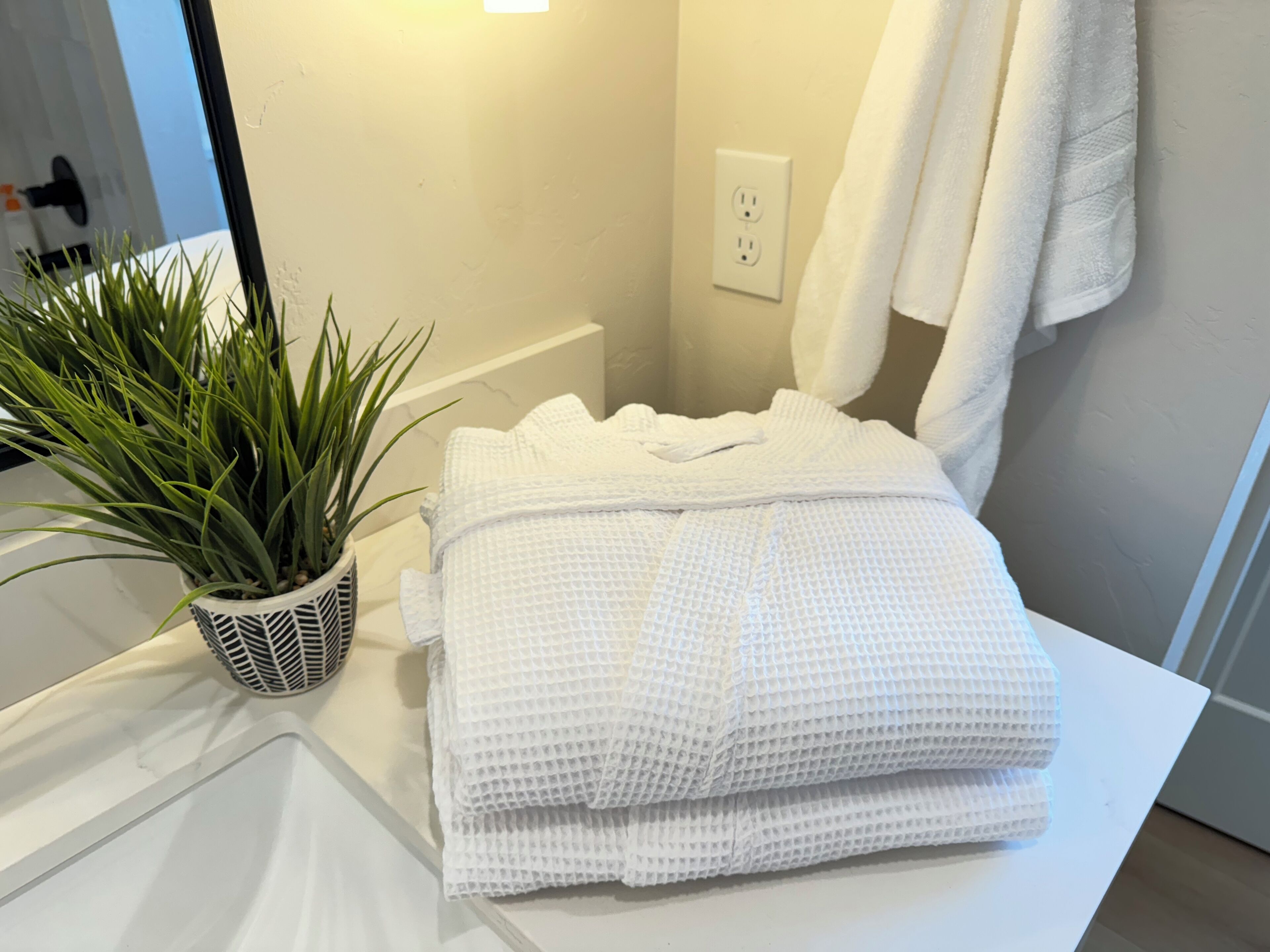 A bathroom with a white sink, a potted plant, a towel, and a mirror.