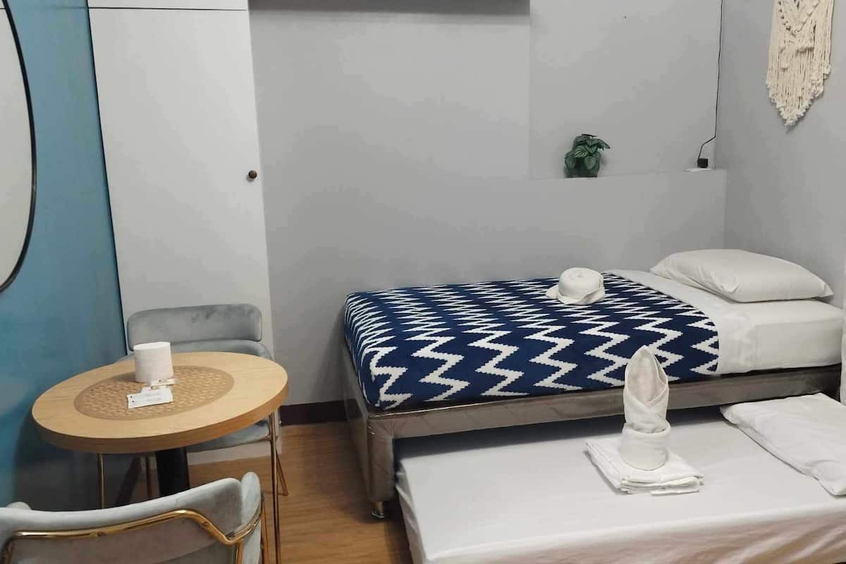 Una habitación pequeña y ordenada con una cama, una silla, una mesita y una planta en maceta.