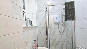 Un bagno con cabina doccia in vetro, lavandino bianco e asciugamano su porta asciugamani.