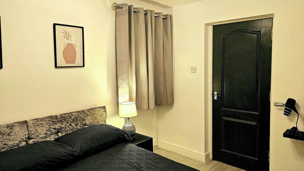 Una camera da letto con un letto, un comodino, una lampada, una porta e un quadro appeso al muro.