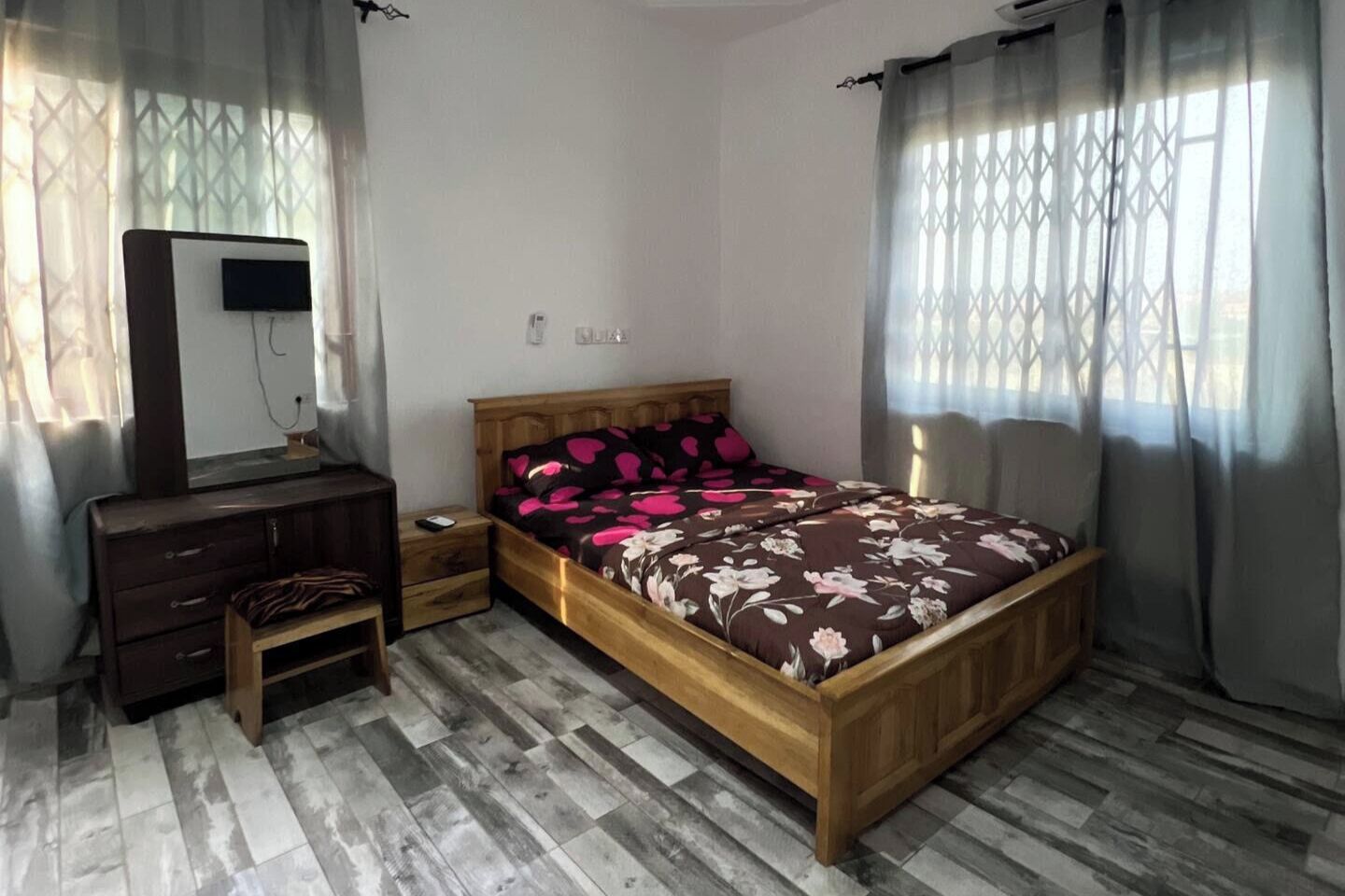 A bedroom with a wooden bed, a dresser, a mirror, and a TV.