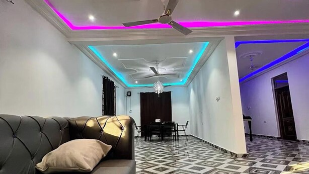 A modern living room with a sofa, a dining area with a chandelier, and a patterned floor. - 5 Bedroom House Sleeps 12 -Balcony -Hired security (Accra)