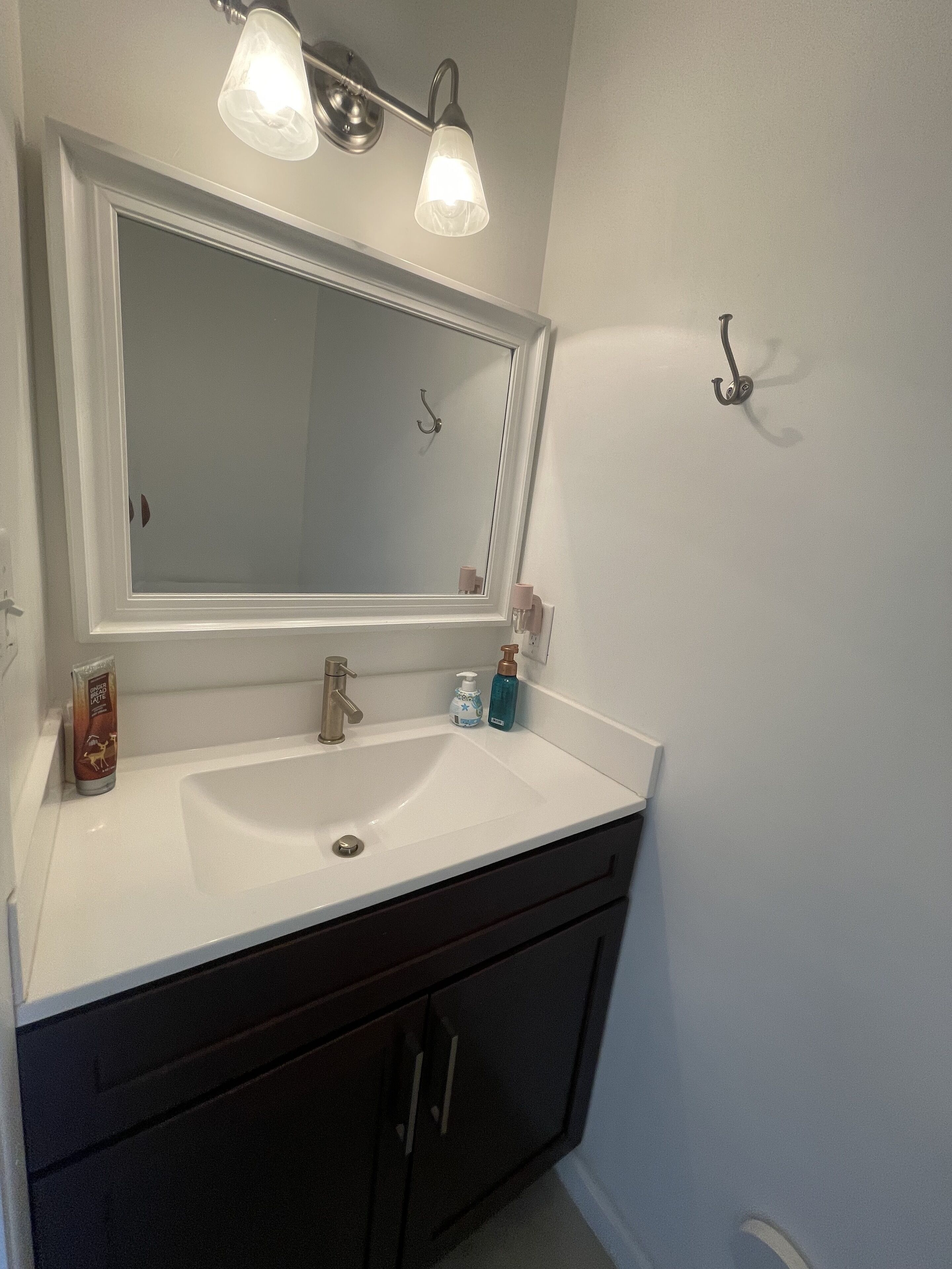 A bathroom with a white sink, dark cabinets, a mirror with two lights, and a towel rack.