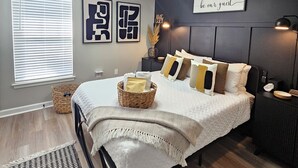 A bedroom with a bed, bedside tables, a wall-mounted light, and a sign saying 'be our guest'. - NEWLY RENOVATED 1100 Sq ft! Bungalow Retreat 5 minutes from Theme Park and Beach (Atlantic City)
