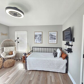 A bedroom with a bed, a hanging chair, a ceiling light, and two framed pictures on the wall.