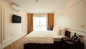 A hotel room with a large bed, a TV mounted on the wall, a bedside table with a lamp, and a window with curtains. - Dolce Mia Home Ninh Binh (Ninh Binh)
