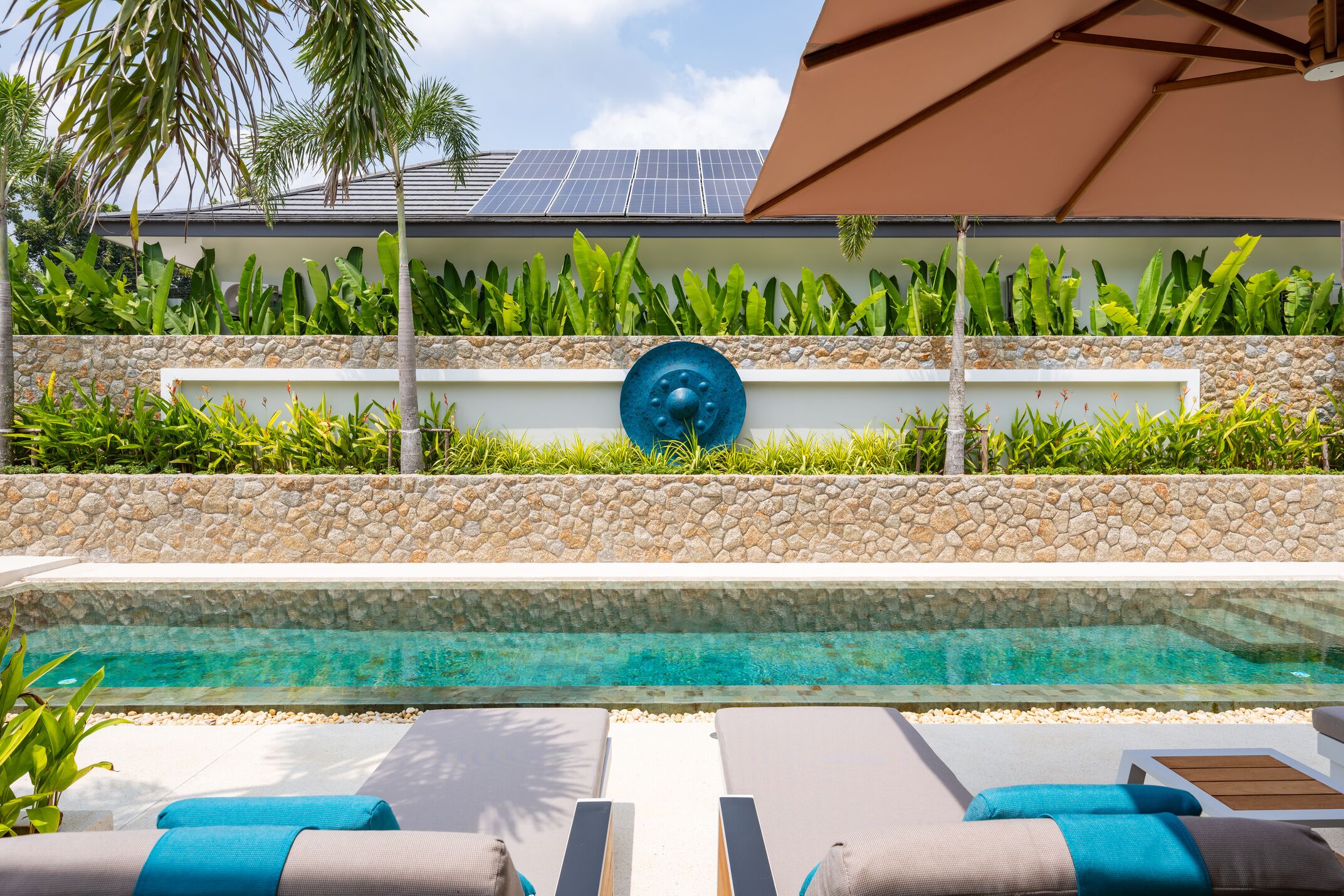 A swimming pool with lounge chairs and a stone wall with greenery.