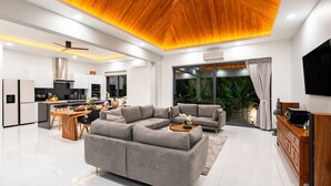 A modern living room with a sectional sofa, a wooden coffee table, and a TV on a wooden cabinet. - Luxury Balinese Private Pool Villa-KBR12 (Koh Samui)