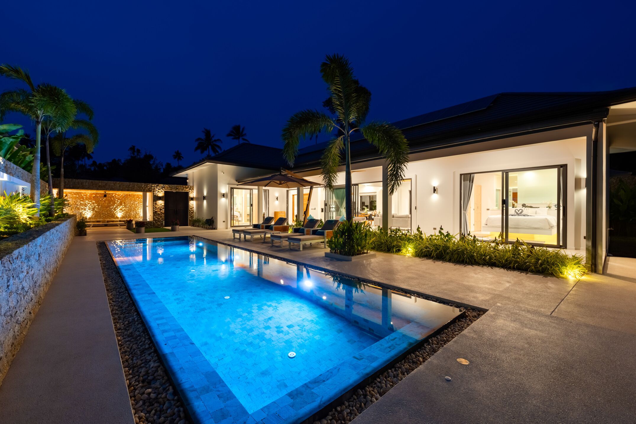 Una casa moderna amb piscina, mobiliari exterior i una zona de pati ben il·luminada.