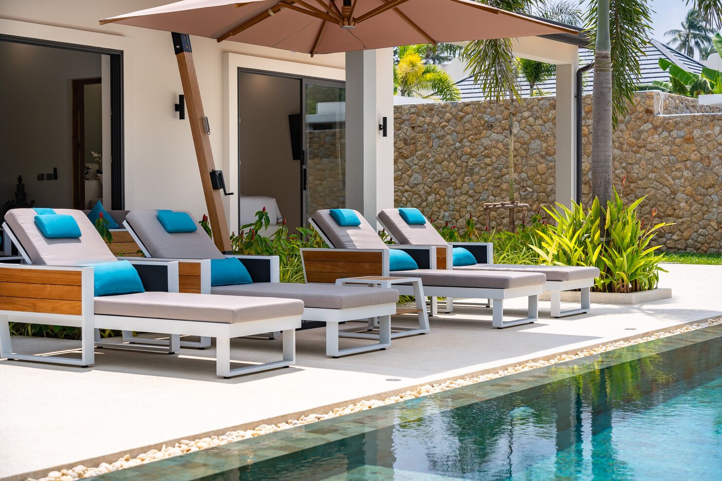 A poolside area with lounge chairs and a stone wall.