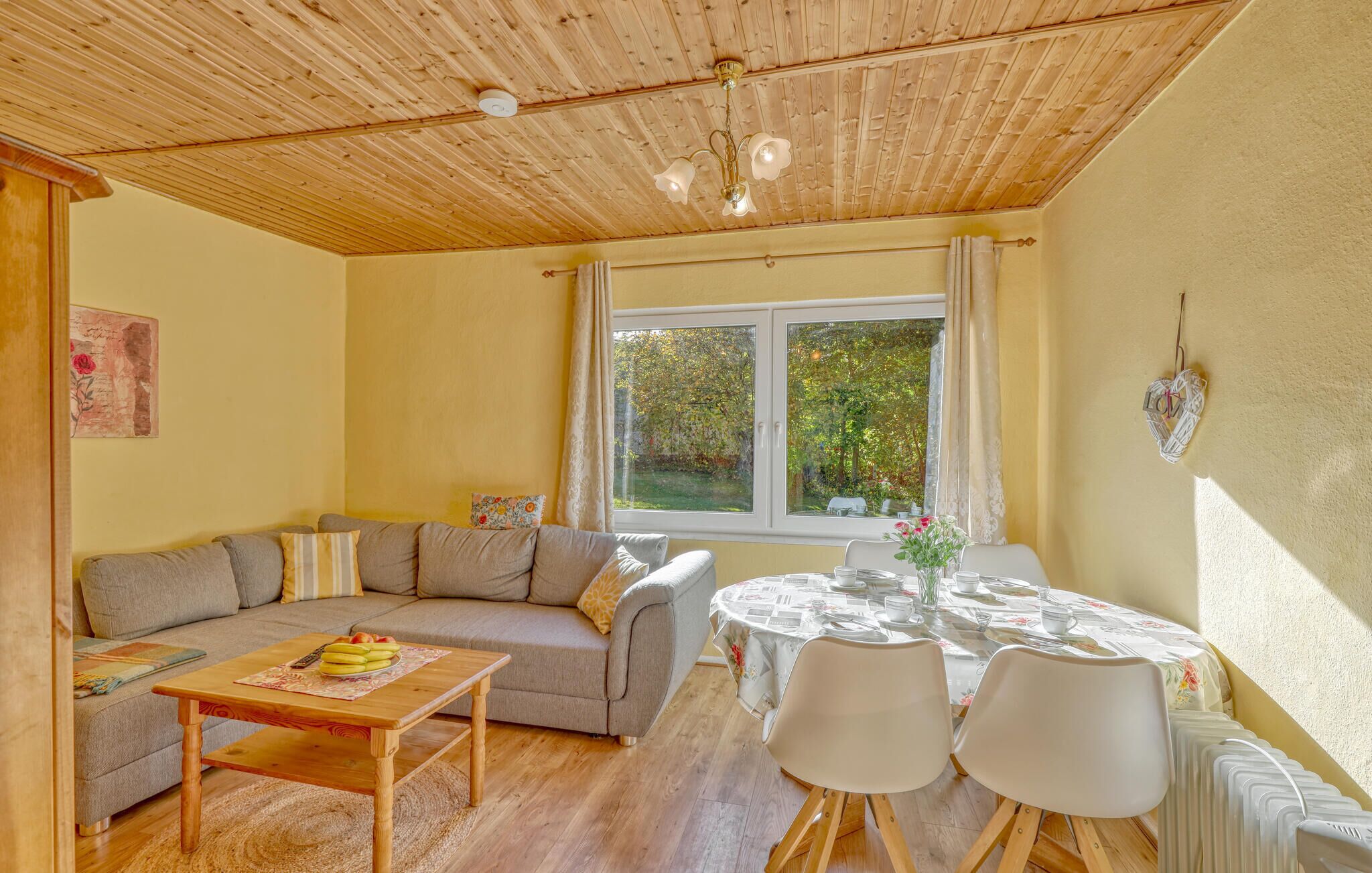 A cozy living room with a wooden ceiling, a sofa, a coffee table, and a dining table with chairs.