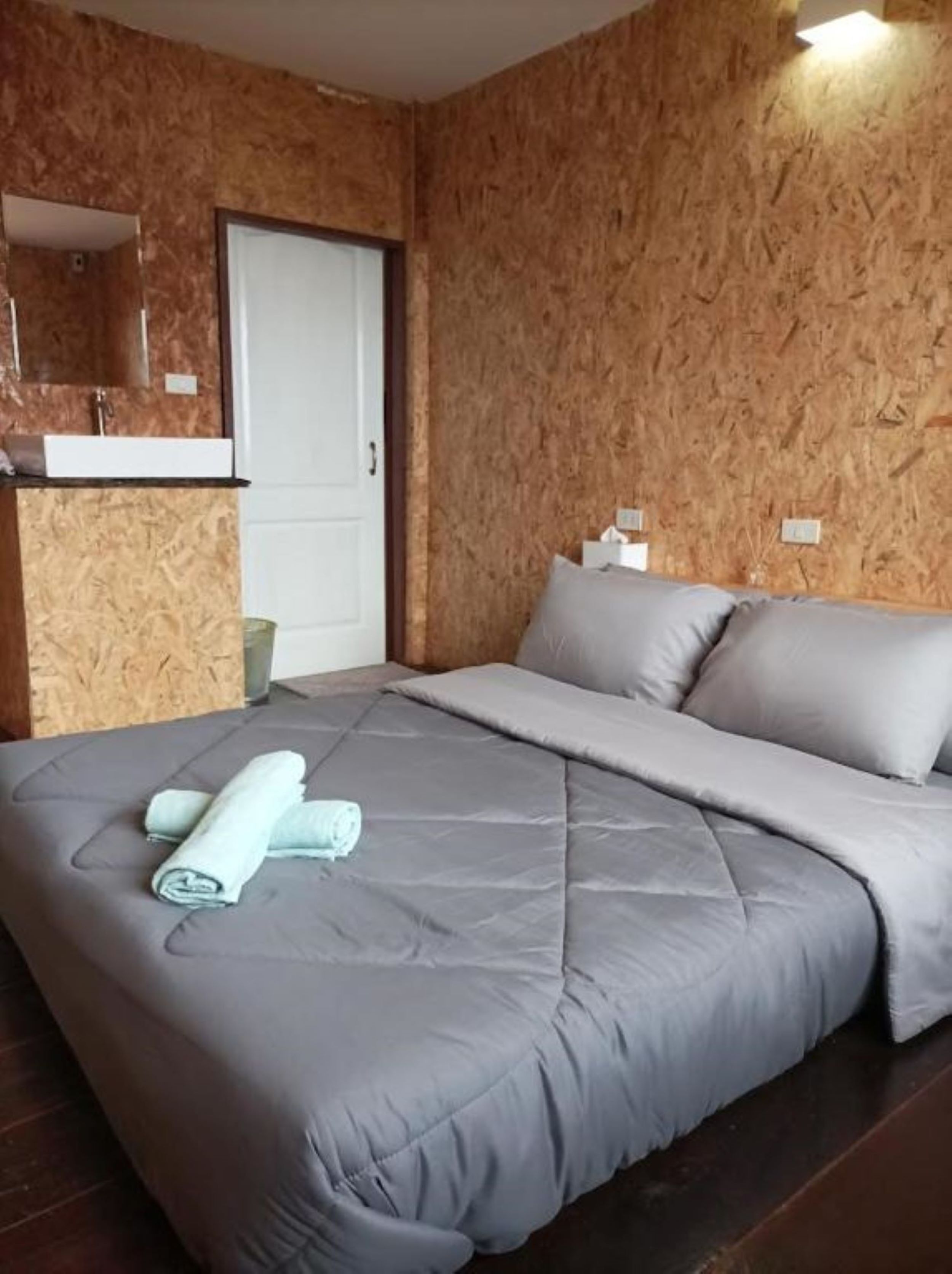 Une chambre avec un mur en bois, un lit avec une literie grise et une petite salle de bain comprenant un miroir et un lavabo.