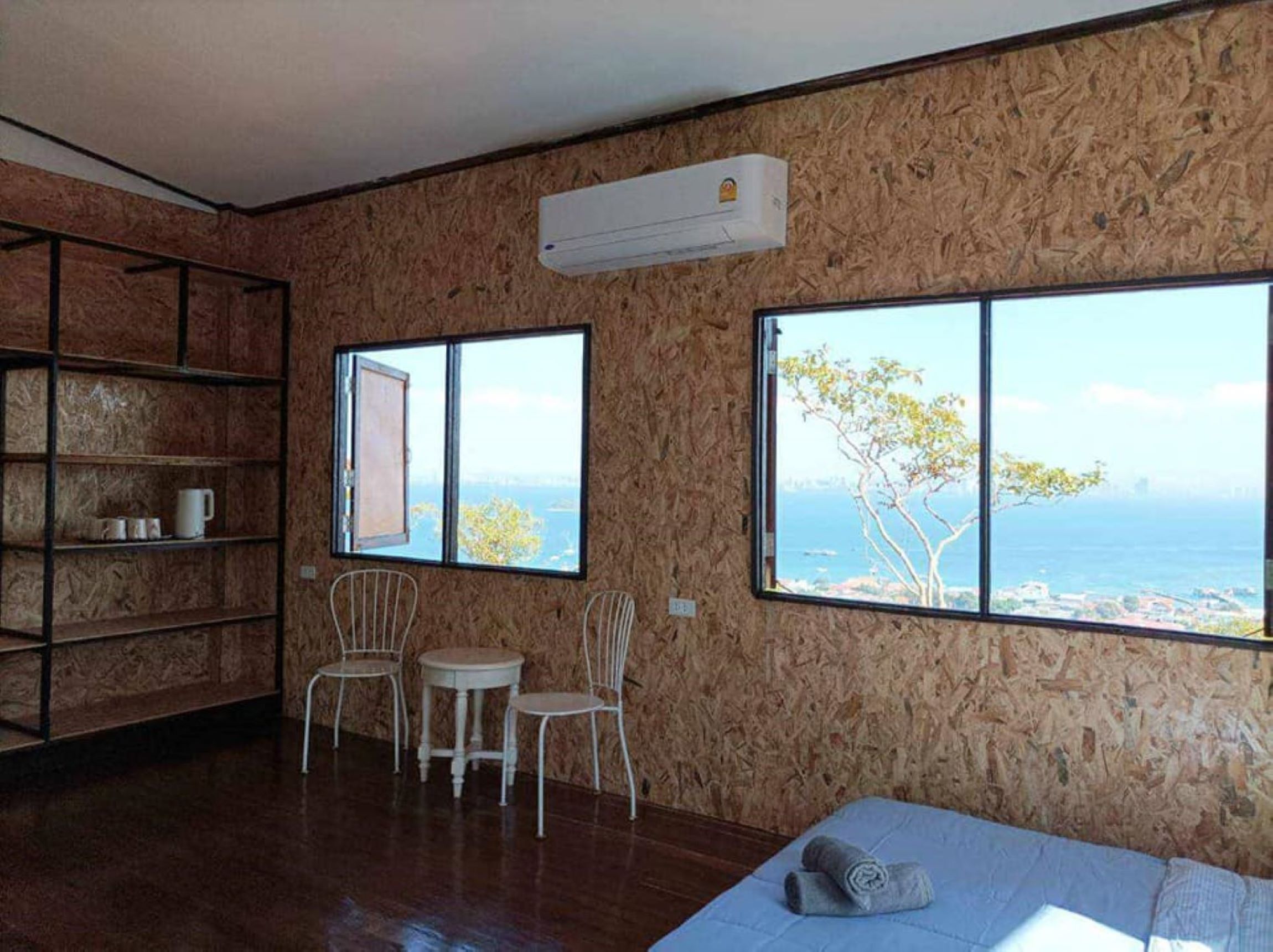 A room with wooden walls, a bed, a small table with chairs, and large windows overlooking the sea.