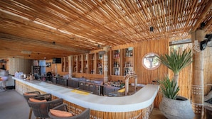 A bar area with a wooden ceiling, bar stools, a large potted plant, and shelves with bottles. - 79 Beach Club and Resort Samui (Koh Samui)