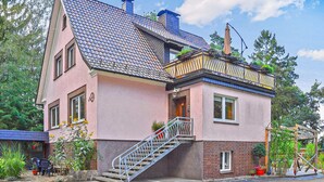 Ein zweistöckiges Haus mit einem geneigten Dach, einem Balkon mit Geländer und einer Treppe, die zum Eingang führt.