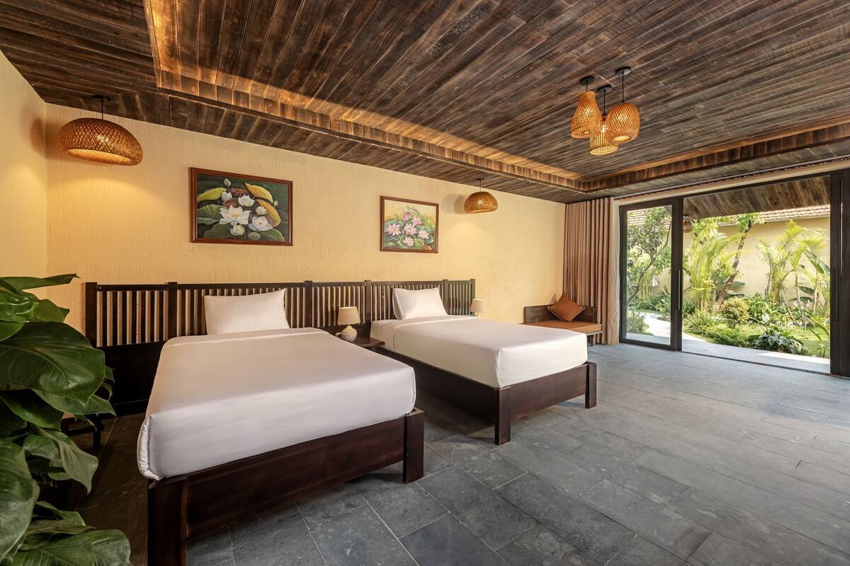 A hotel room with two beds, wooden ceiling, large windows, and tropical artwork.