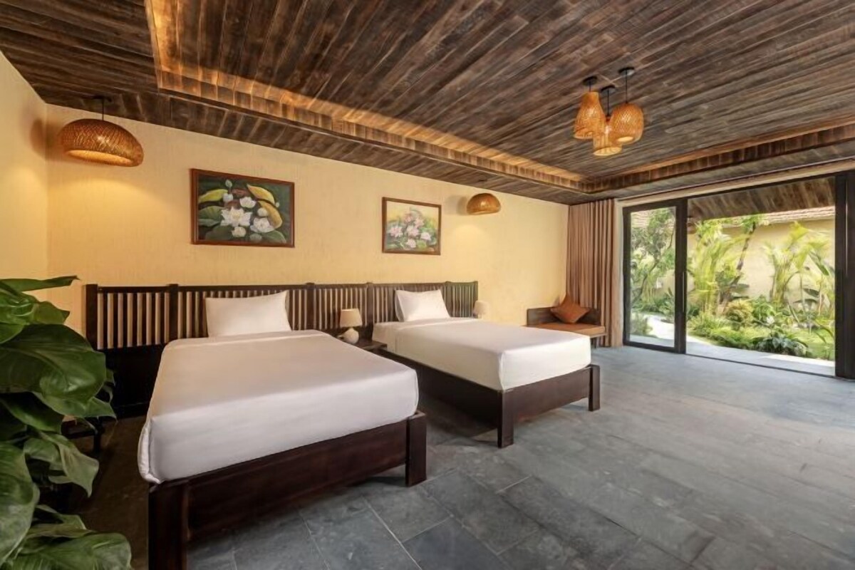 Habitación de hotel con dos camas, cabeceros de madera, ventanas amplias y vista a zonas verdes.