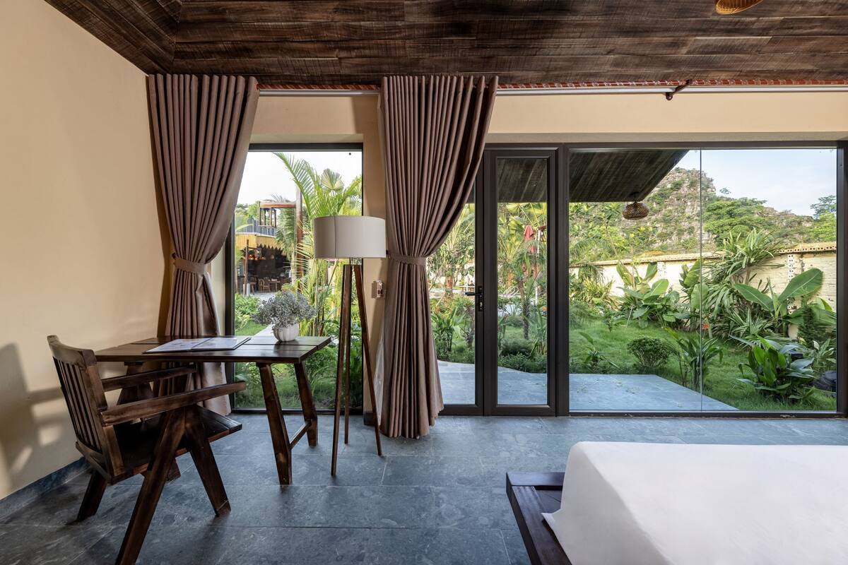 A room with a bed, a table, and a chair, a lamp, and curtains.