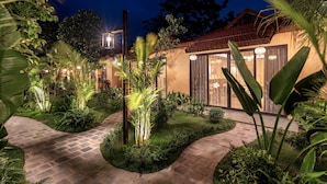 A well-lit garden pathway leading to a building with large windows and a tiled roof.