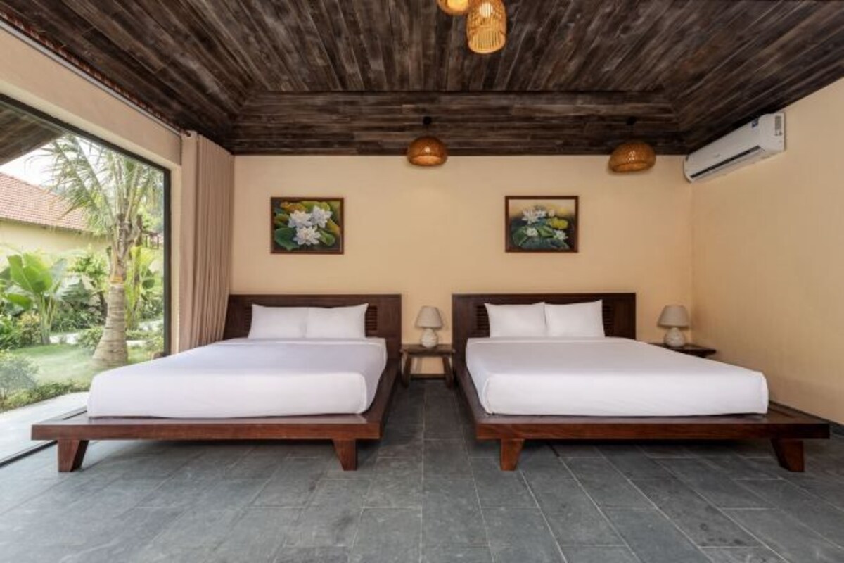 Una habitación con dos camas, cabeceros de madera, un ventanal con vistas a zonas verdes y dos lámparas fijadas a la pared.
