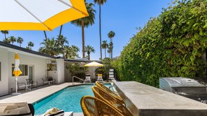 A poolside area with lounge chairs, a barbecue grill, and a pool.