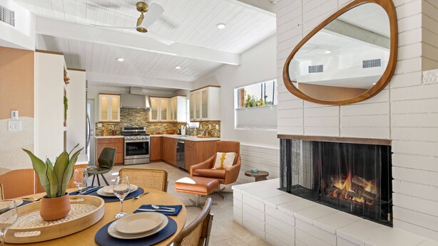 A modern kitchen with white cabinets, a dining area with a wooden table, and a fireplace.