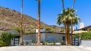 A modern house with a garage, surrounded by palm trees and a hilly landscape.