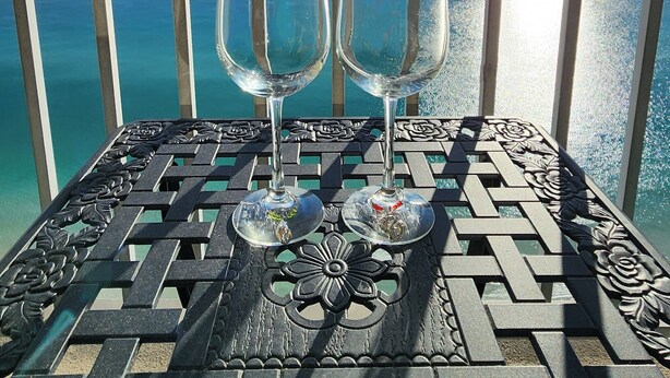 A balcony with a metal railing and a table with two wine glasses. - Direct Beachfront Condo Near Pier Park! 2BD+Bunk 3BA, 2 Free Parking! (Panama City Beach)