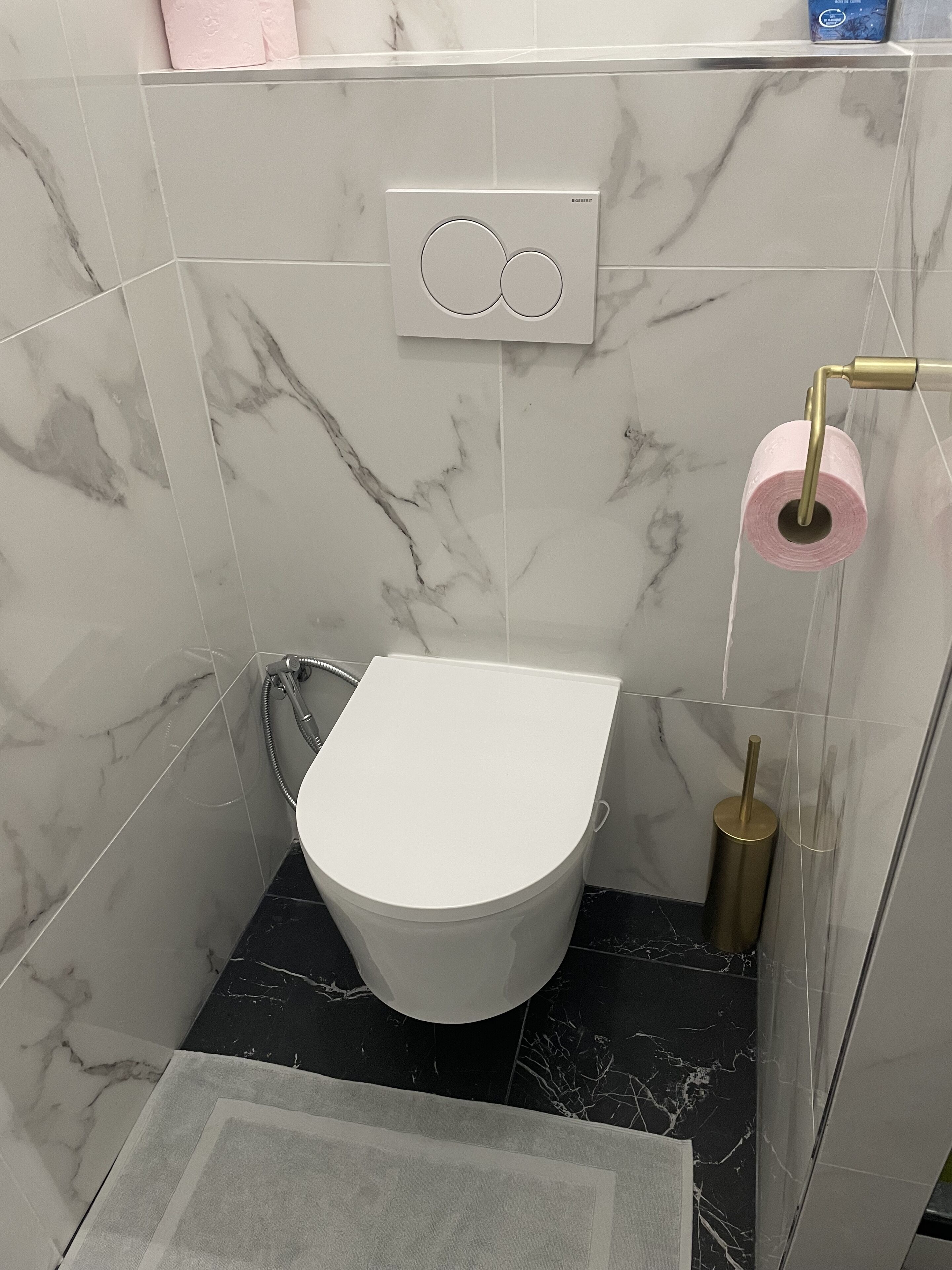 Moderni kylpyhuone, jossa on valkoinen wc-istuin, marmorilaatat, suihku ja wc-paperiteline.