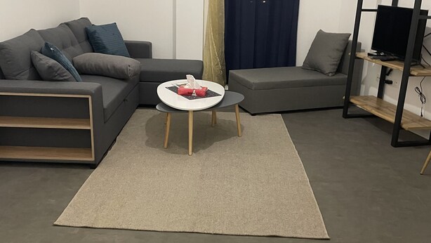 Ein modernes Wohnzimmer mit einem grauen Sofa, einem runden Couchtisch und einem Fernseher auf einem Holzboden.