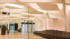 Un hall d’entrée spacieux au design moderne, comprenant un espace détente avec des canapés de couleur marron foncé et une cloison en verre.