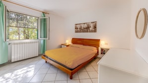 Een slaapkamer met een bed, twee nachtkastjes, een radiator, een raam met gordijnen en een aan de muur hangend schilderij.
