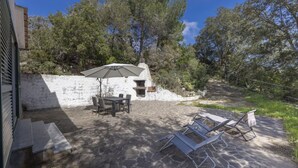 Een terras buiten met stenen vloer, een tafel, stoelen, een barbecue en een parasol.