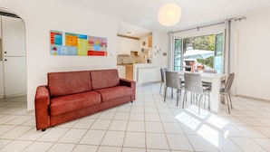 Een moderne woonkamer met een rode bank, een eethoek met stoelen, een keuken op de achtergrond en een groot raam met een paraplu.