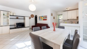 Een moderne keuken met witte kasten, een eettafel met stoelen en een televisie op een zwart dressoir.