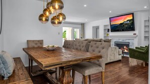 Ein modernes Wohnzimmer mit einem Holzesstisch, einer Couch und einem Fernseher über einem Kamin.