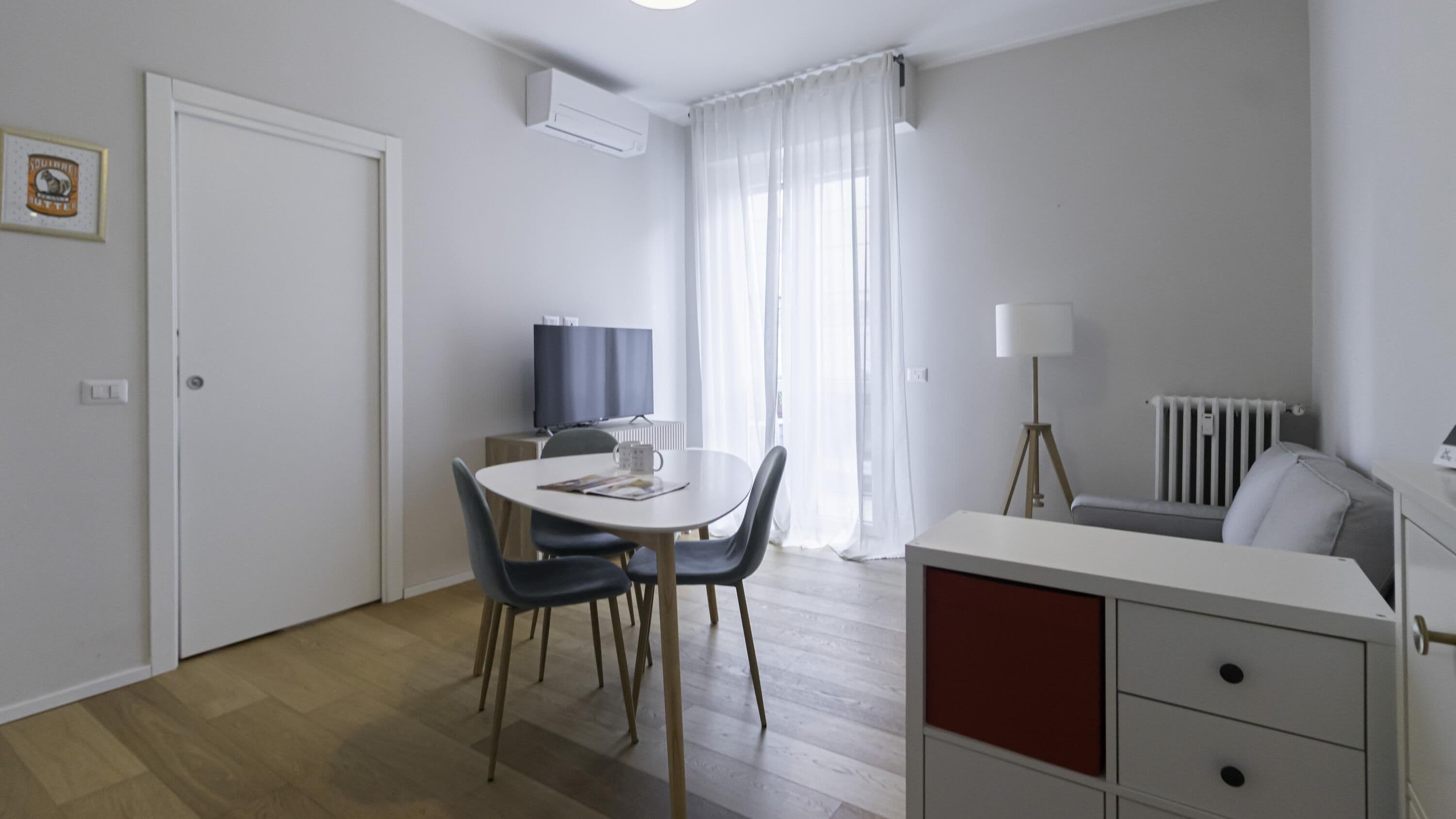 A modern, well-lit room with a dining table, chairs, a TV, a lamp, and a radiator.
