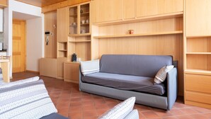 Un salon chaleureux avec un canapé gris, des coussins à motifs, des étagères en bois et un sol carrelé.