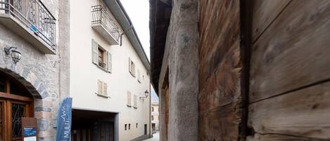 A narrow cobblestone street with buildings on either side, featuring a wooden door and a sign that reads "Benvenuti Welcome."