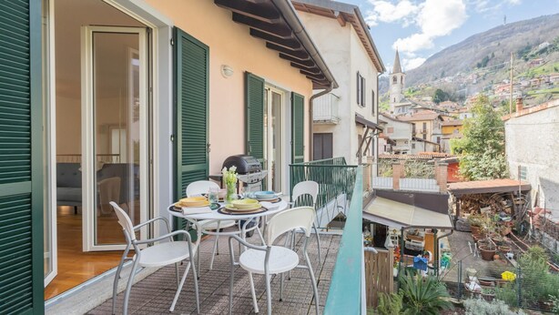 A balcony with a table and chairs, a grill, and a view of a village with a church. - Ponente Balcony Garden (Gravedona)