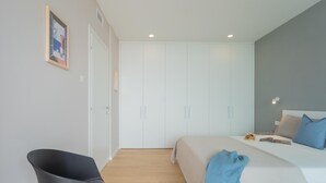 Een slaapkamer met een bed, nachtkastje en een stoel. Er staat een garderobe met spiegel en een deur.