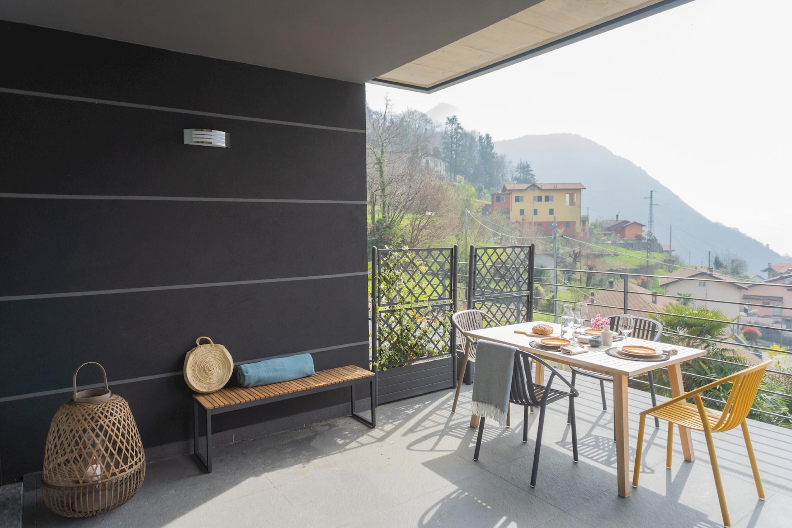 A balcony with a table set for dining, a bench, and a wicker lantern.
