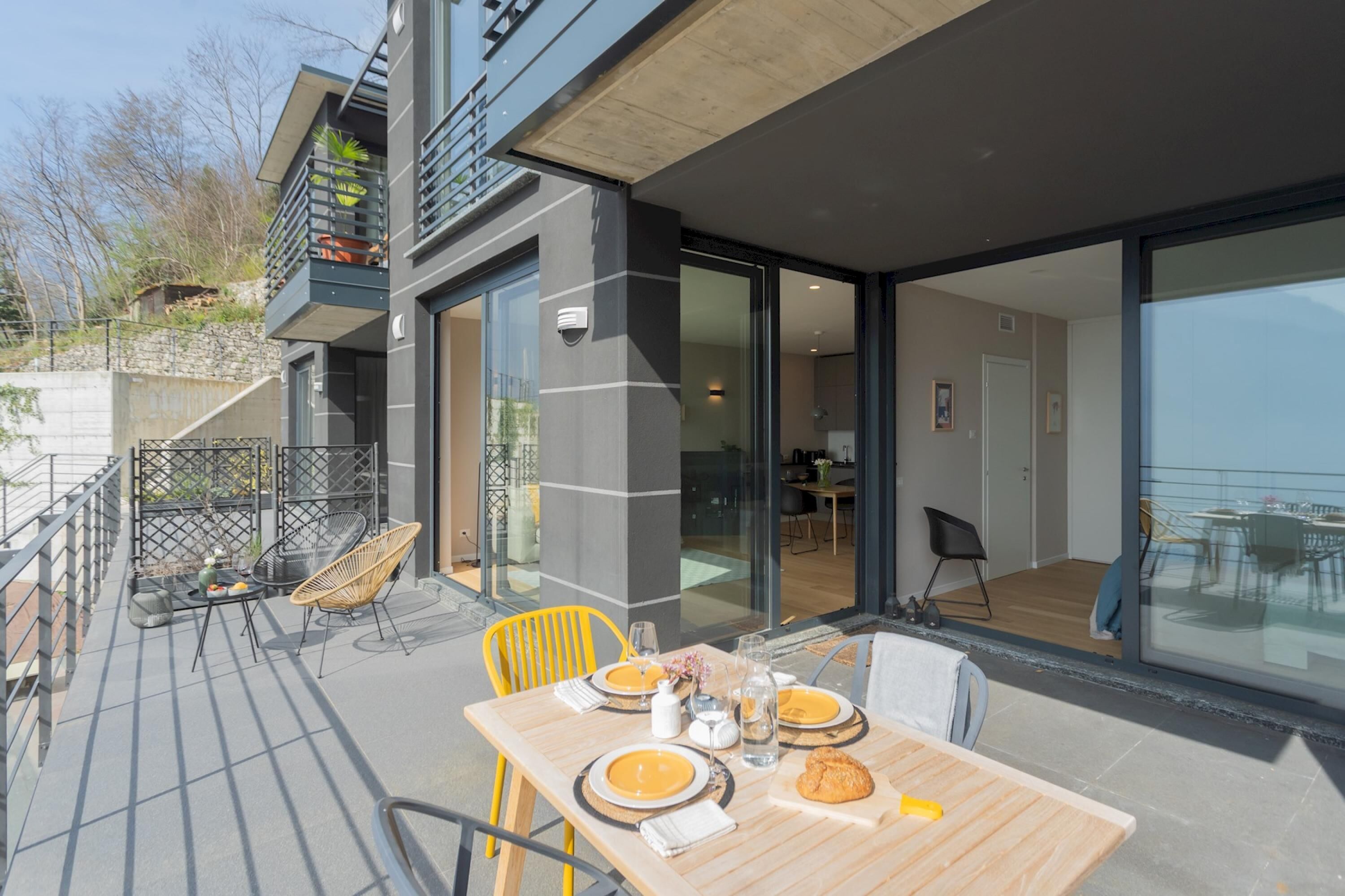 Un espace de restauration extérieur moderne, avec une table en bois dressée pour deux personnes, entourée de chaises jaunes.