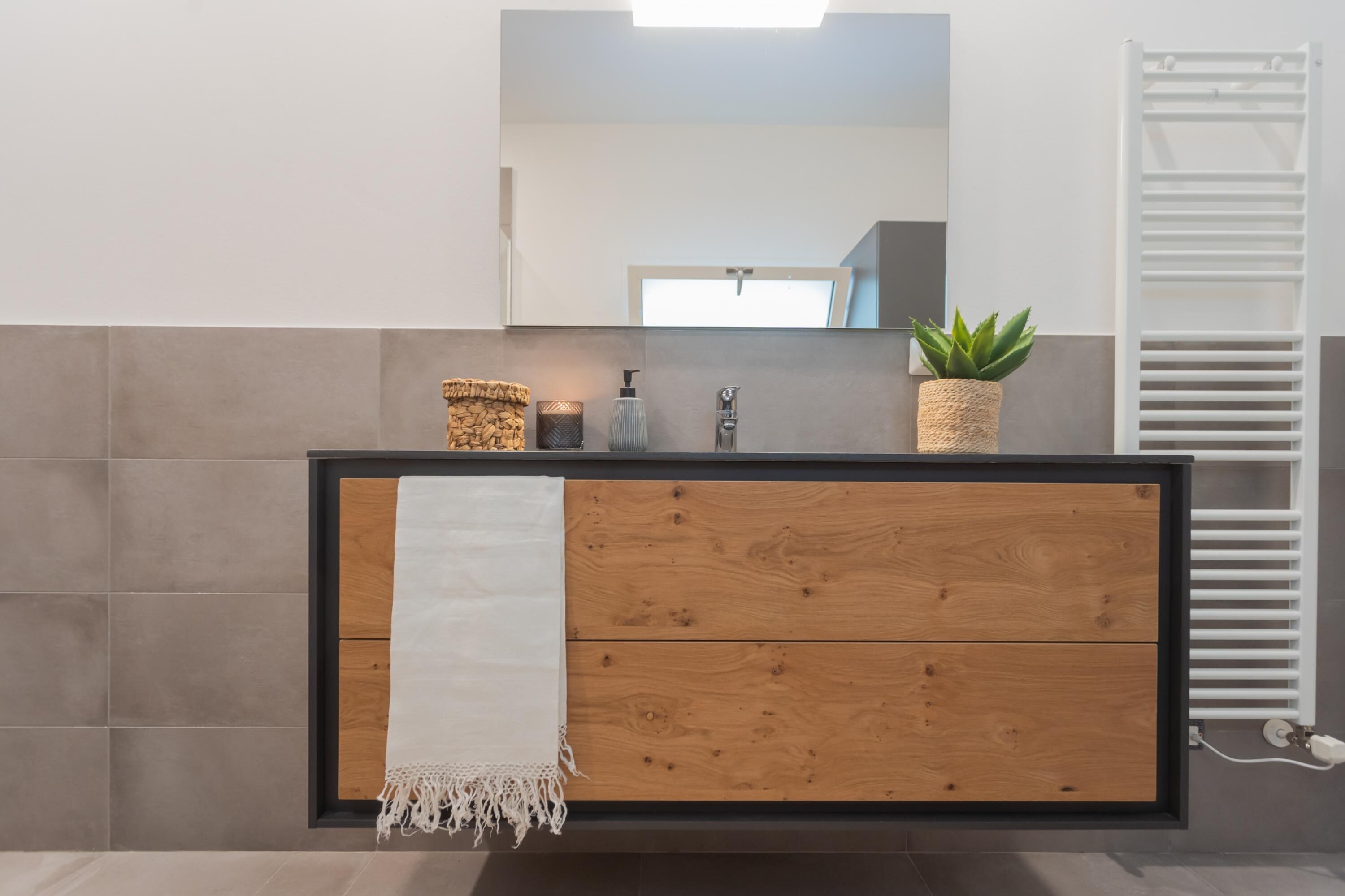 Un baño moderno con tocador de madera, un espejo, una toalla, una planta y un perchero para toallas.