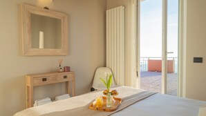 A hotel room with a bed, a wooden bedside table, a mirror, a chair, and a balcony with a view. - Sunset Terrace Loft Best View on Como (Brunate)