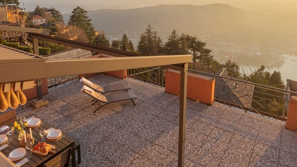 A rooftop terrace with a table set for dining, overlooking a scenic valley and distant mountains. - Sunset Terrace Loft Best View on Como (Brunate)