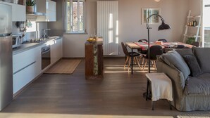A modern kitchen with white cabinets, a dining area with a table and chairs, and a living room with a sofa and a lamp. - Sunset Terrace Loft Best View on Como (Brunate)