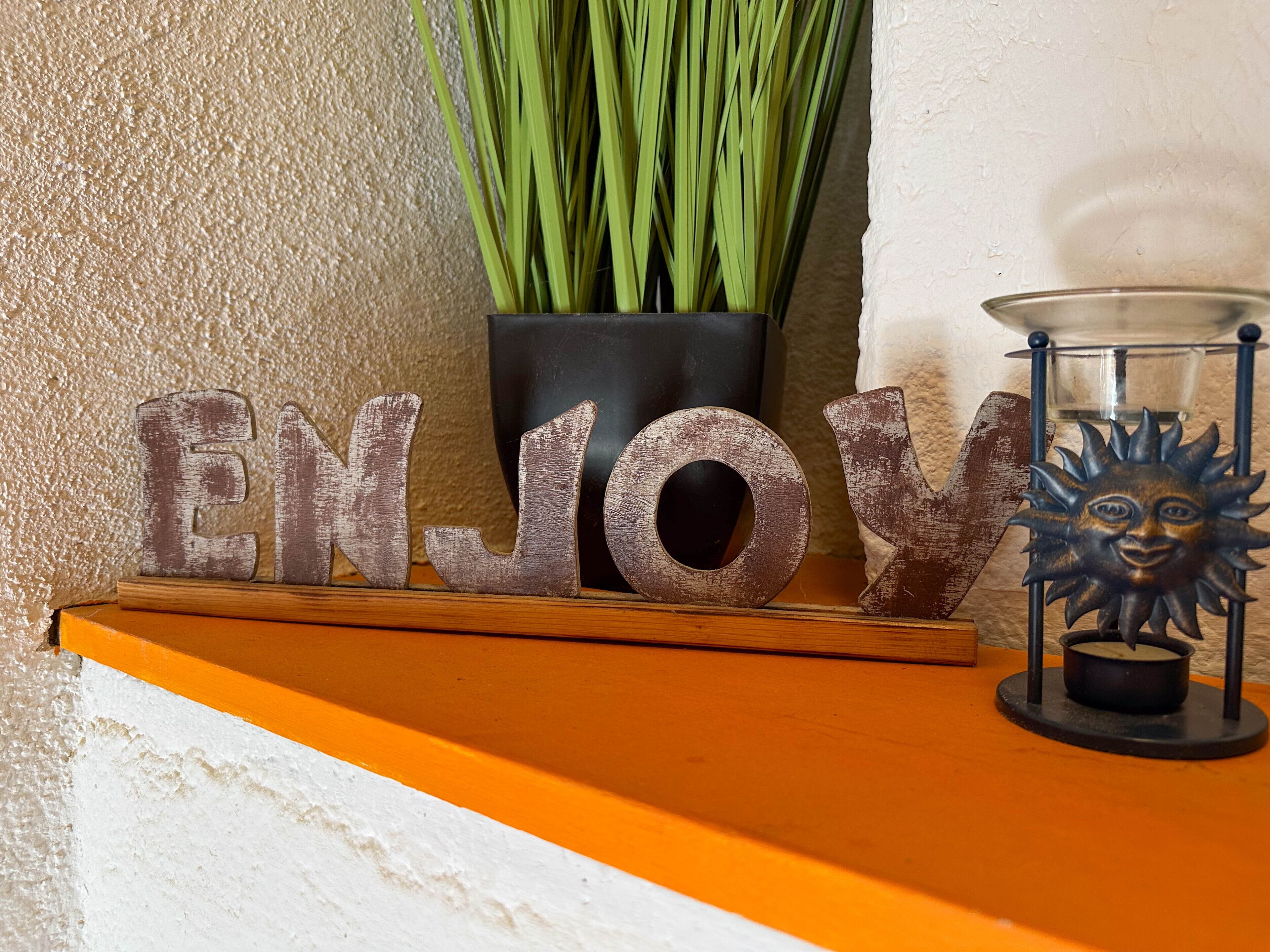 A decorative sign with the word "ENJOY" and a sun-shaped candle holder on a shelf.