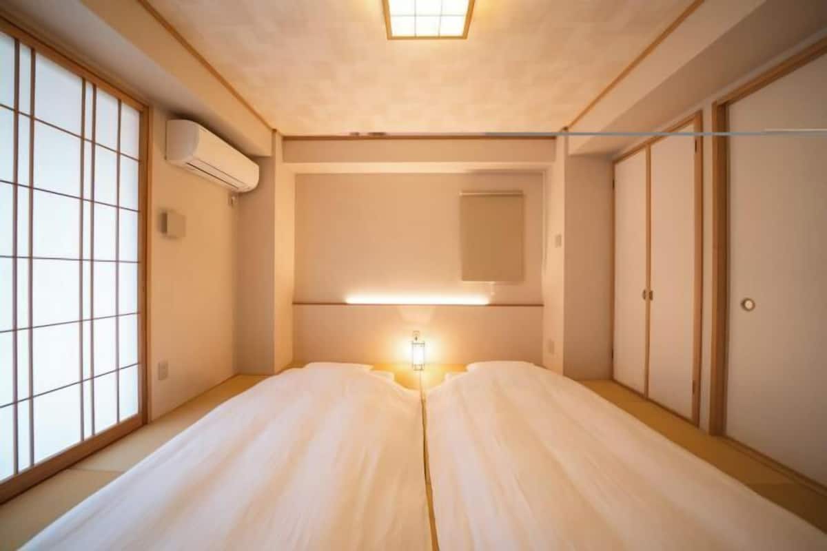 Una habitación japonesa tradicional con suelo de tatami, puertas correderas, ventilador de techo y mesita de noche.